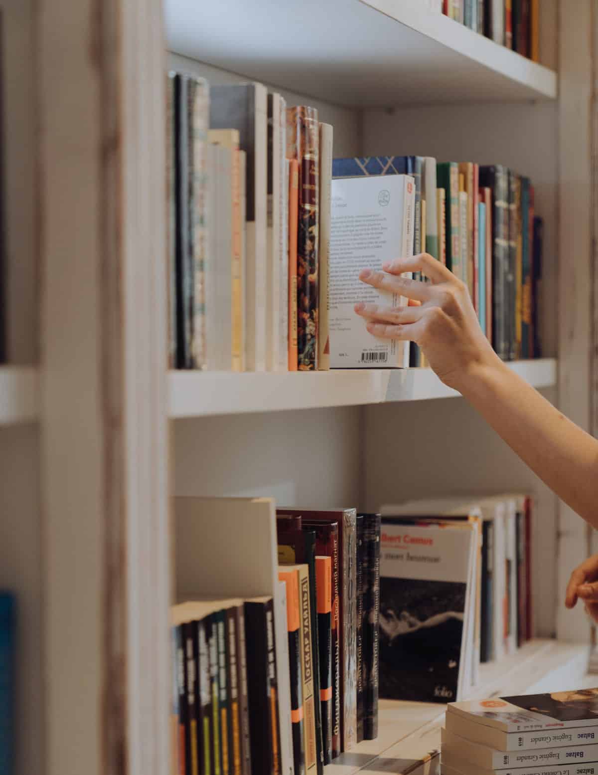 Person reaching up to out book back on a shelf with multiple books.